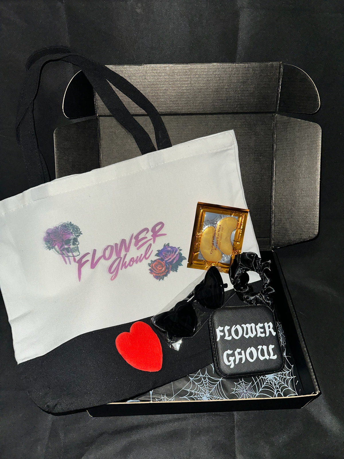 Cursed & Crowned Flower Ghoul gift set featuring a canvas tote, heart sunglasses, scrunchie, sponge, and eye masks.